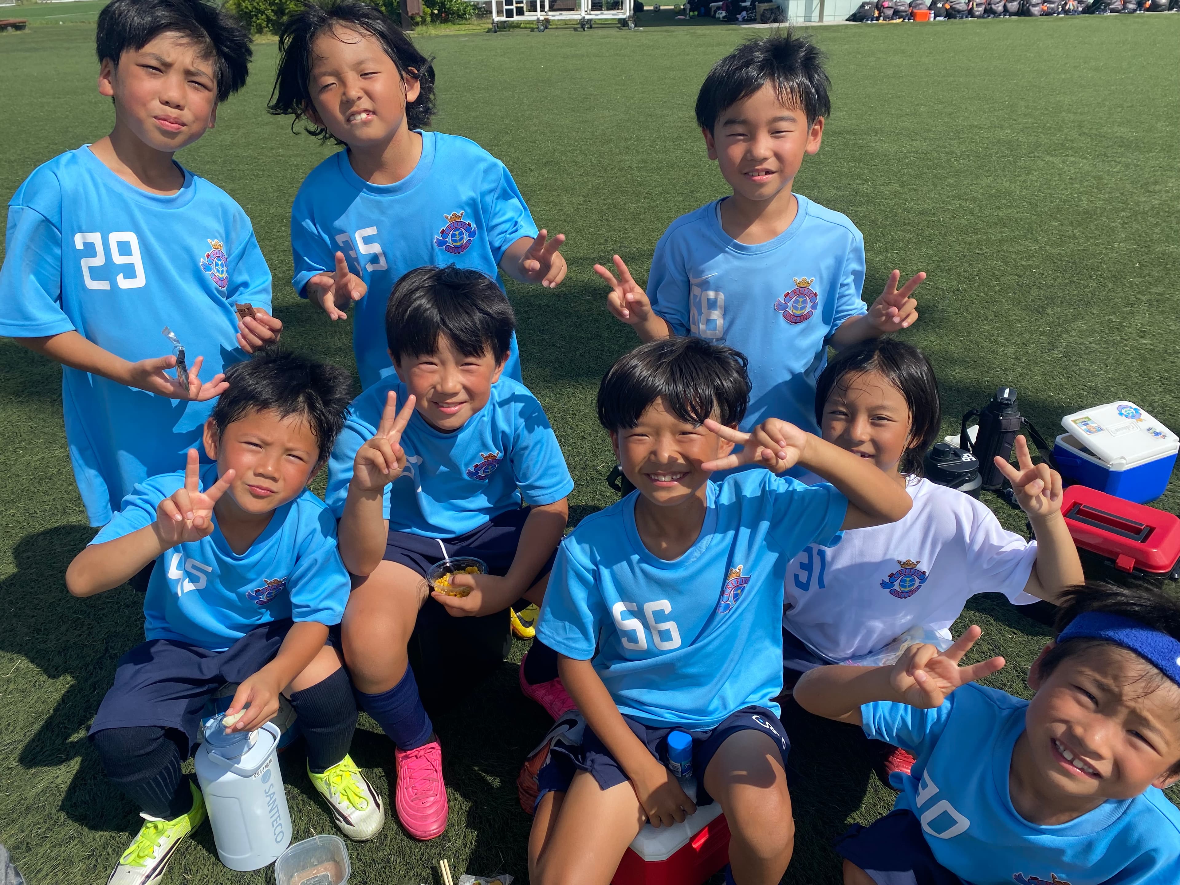 小学生年代の選手たちが休憩中にピースサインで笑う様子
